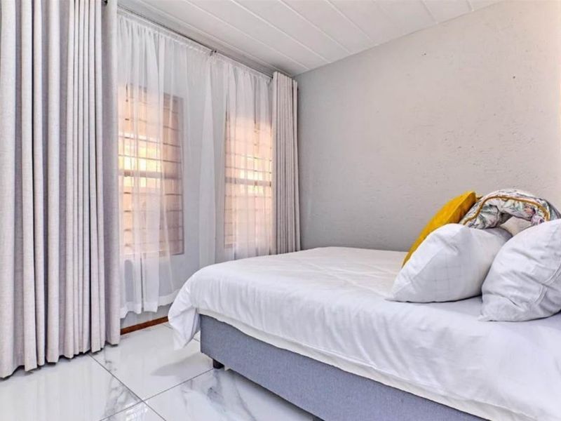A bright bedroom featuring modern white marble-look floor tiles and a clean, neutral aesthetic with ample natural light.