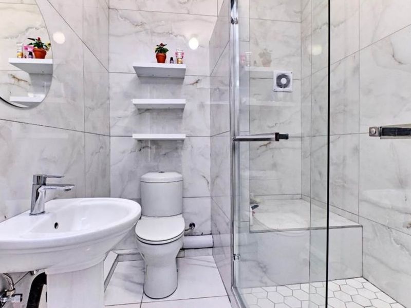 Modern bathroom featuring marble-effect wall tiling, a pedestal washbasin, a toilet, and a glass-enclosed shower with hexagonal floor tiles.