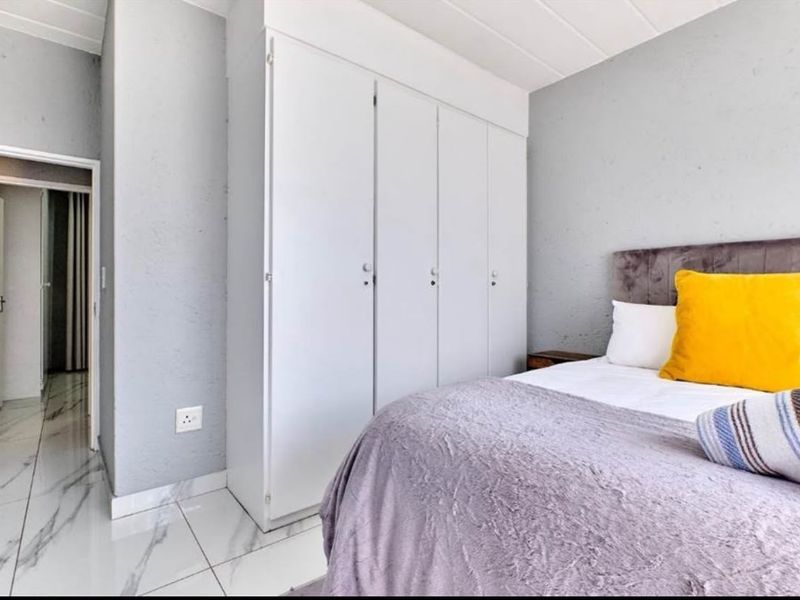 A bedroom featuring built-in cupboards and modern marble-look tiled flooring, providing a clean and functional living space.