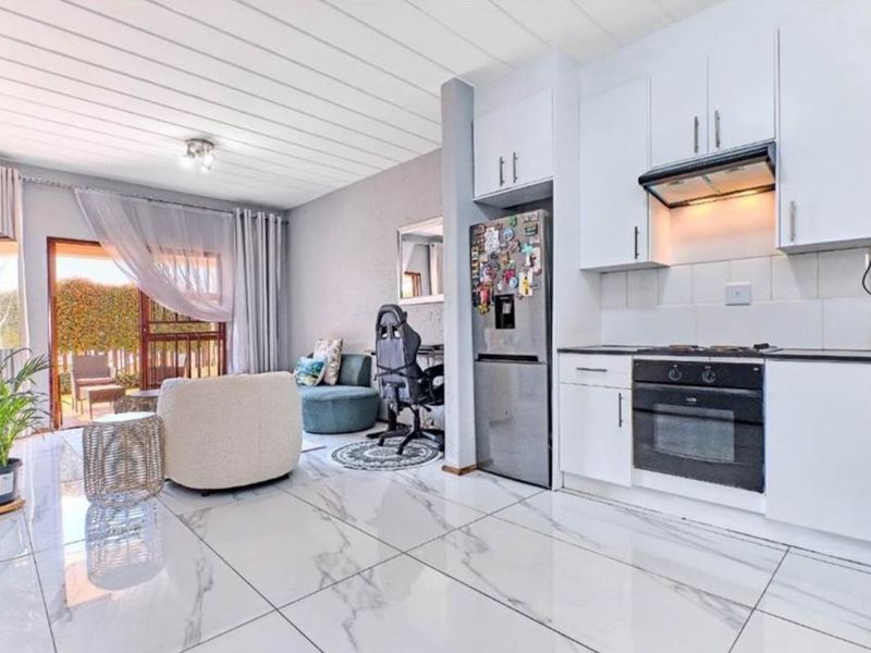 Open-plan living area featuring a modern kitchen with white cabinetry, built-in oven, hob, and sleek marble-look floor tiles leading to a patio.