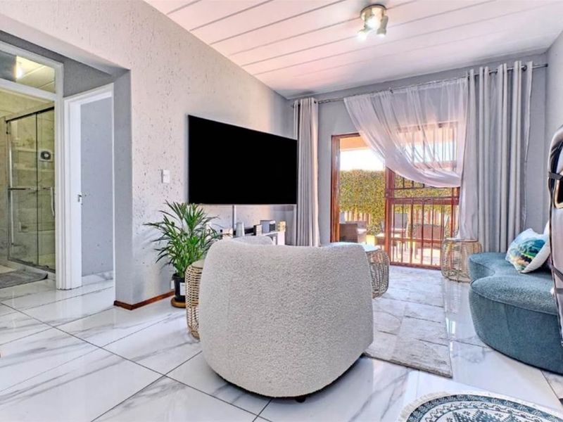 A bright living room featuring large marble-look floor tiles, textured walls, and a sliding glass door providing access to an outdoor area.