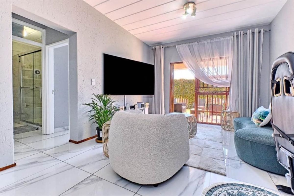 A bright living room featuring large marble-look floor tiles, textured walls, and a sliding glass door providing access to an outdoor area.