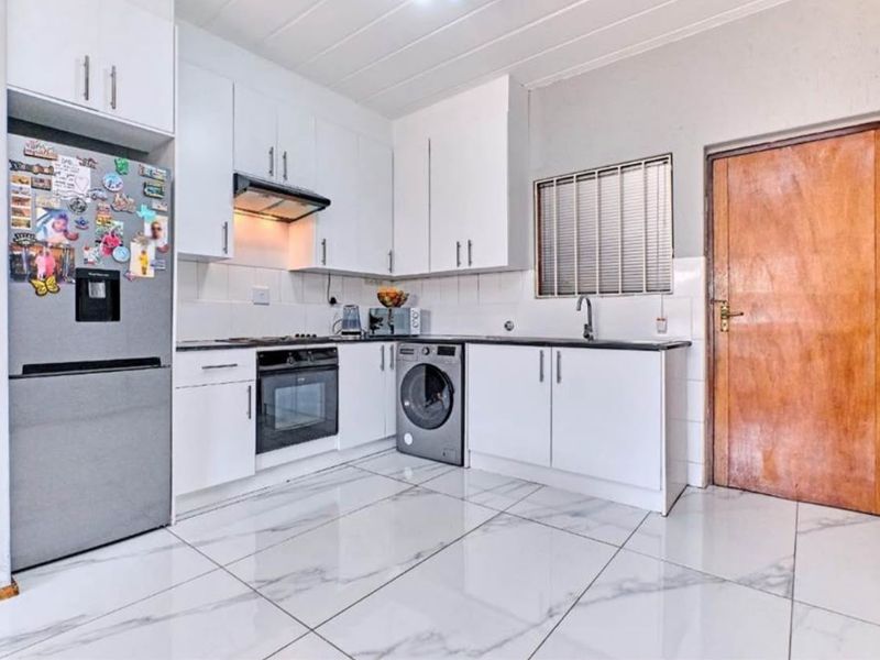 A functional kitchen featuring white cabinetry, built-in oven and hob, extractor fan, sink, and modern marble-look tiled flooring.
