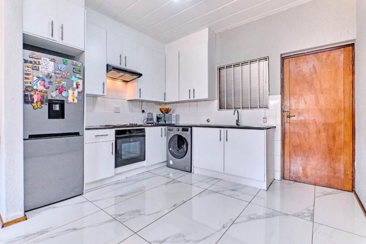 A functional kitchen featuring white cabinetry, built-in oven and hob, extractor fan, sink, and modern marble-look tiled flooring.