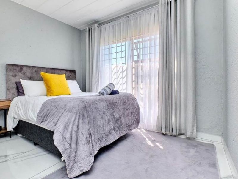 A well-lit bedroom featuring tiled flooring and a large sliding glass door with integrated security gate, providing access to the exterior.