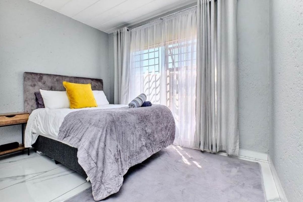 A well-lit bedroom featuring tiled flooring and a large sliding glass door with integrated security gate, providing access to the exterior.