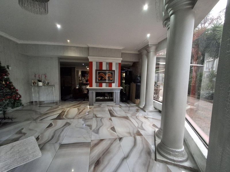 Spacious living area featuring large format patterned floor tiles, a central fireplace with decorative surround, and prominent architectural columns overlooking the garden.