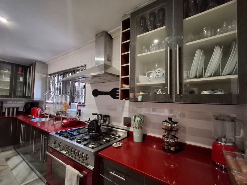 Modern kitchen featuring bold red countertops, stainless steel gas range with extractor fan, and ample dark-toned cabinetry with glass-fronted display sections.