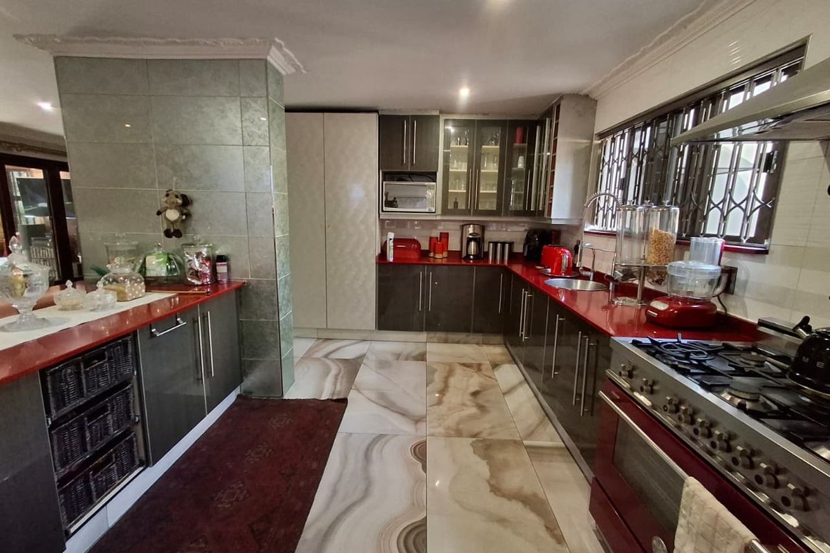 A well-appointed kitchen featuring dark cabinetry, red countertops, a gas stove with oven, and large format decorative floor tiles.