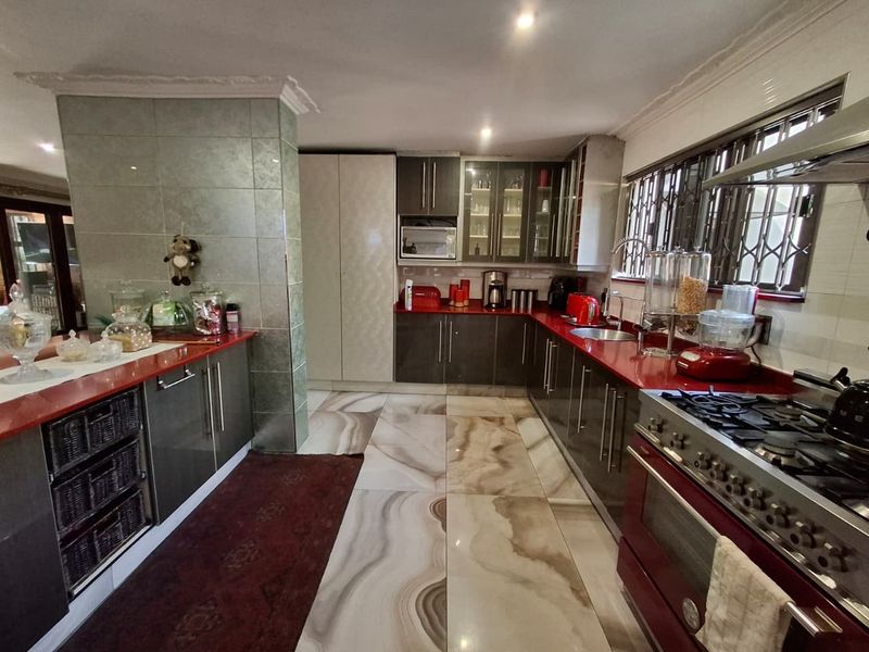 A well-appointed kitchen featuring dark cabinetry, red countertops, a gas stove with oven, and large format decorative floor tiles.