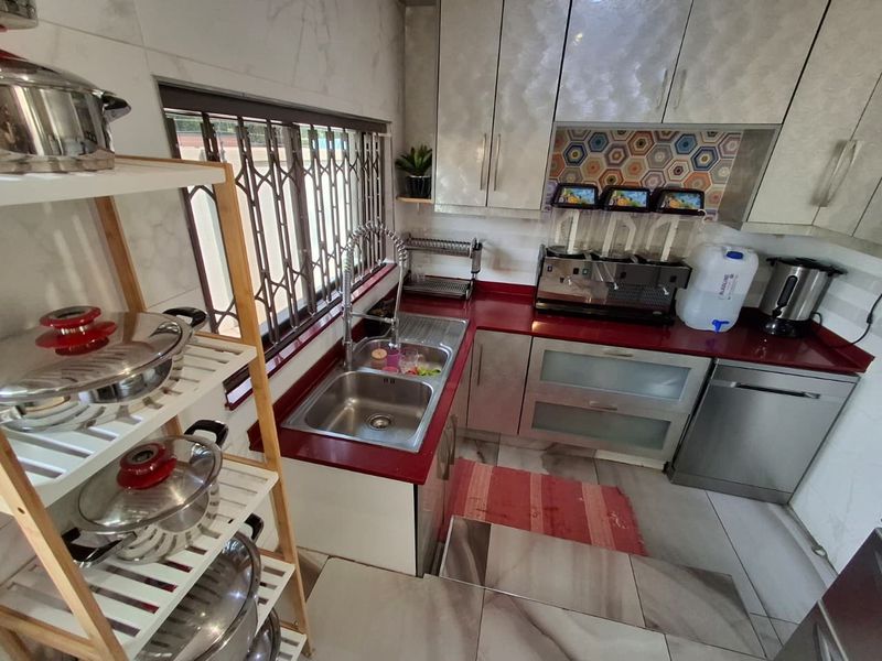 A functional kitchen featuring red stone countertops, double basin sink, built-in cabinetry, and a decorative hexagonal tiled backsplash.