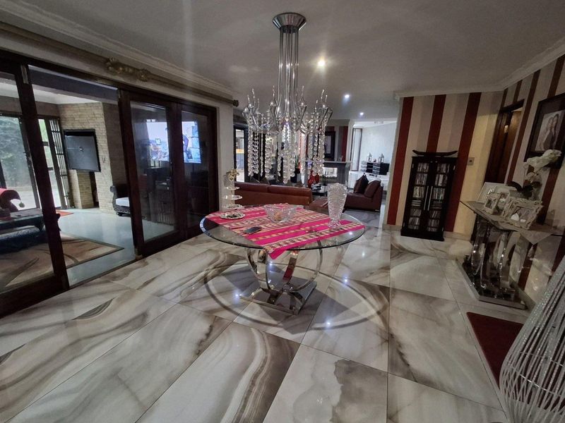 Spacious dining area featuring large format polished floor tiles, a statement crystal chandelier, and sliding glass doors leading to an outdoor patio space.