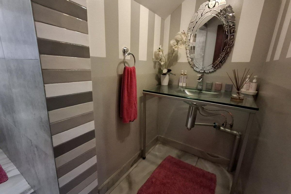 A compact bathroom featuring a modern glass vanity, wall-mounted faucet, and a tiled shower enclosure with striped accent wall detailing.