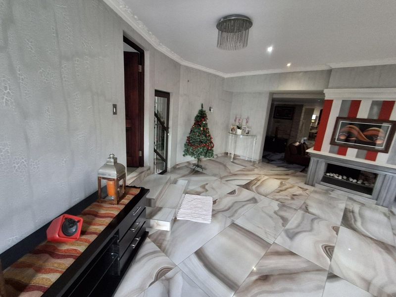 Spacious living area featuring distinctive marble-effect floor tiles, a built-in fireplace, and decorative ceiling detailing, offering a bright and open layout.