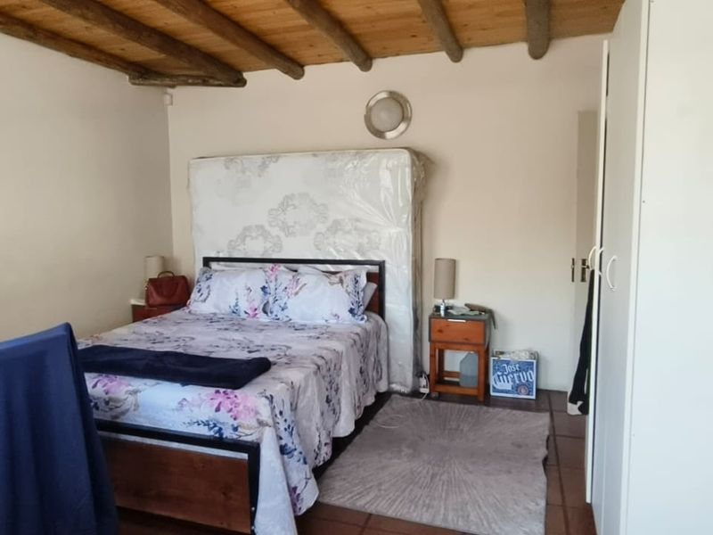 A bedroom featuring exposed timber ceiling beams, terracotta floor tiles, and a built-in wardrobe, offering a rustic aesthetic with functional storage space.