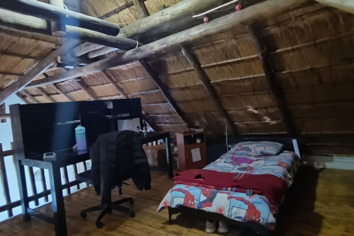 A rustic loft-style bedroom featuring exposed timber roof trusses, a traditional thatched ceiling, and warm timber flooring.