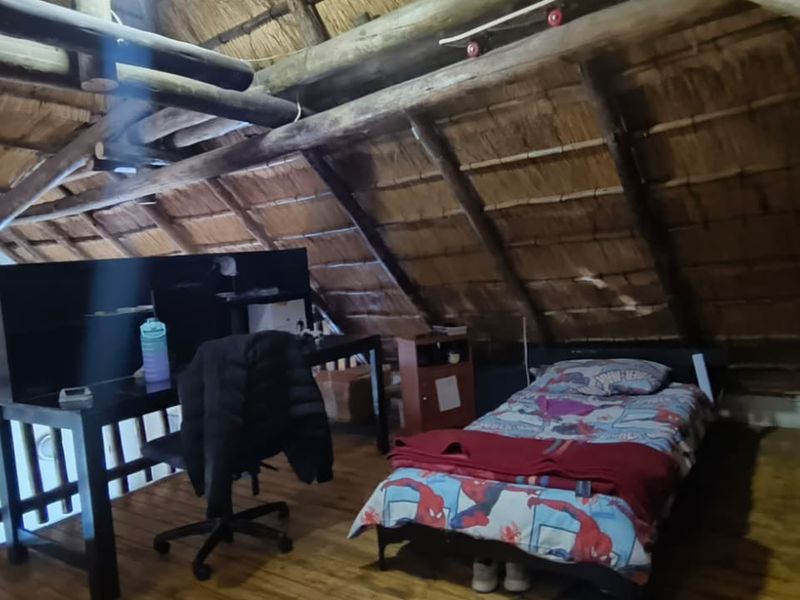 A rustic loft-style bedroom featuring exposed timber roof trusses, a traditional thatched ceiling, and warm timber flooring.