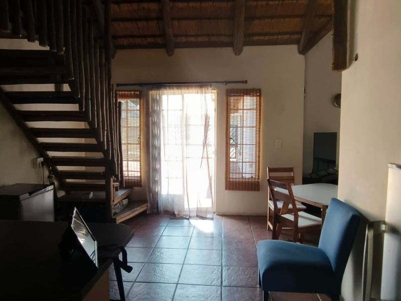Open plan living area featuring exposed timber staircase, thatched ceiling with timber trusses, and tiled flooring leading to a sliding glass door.