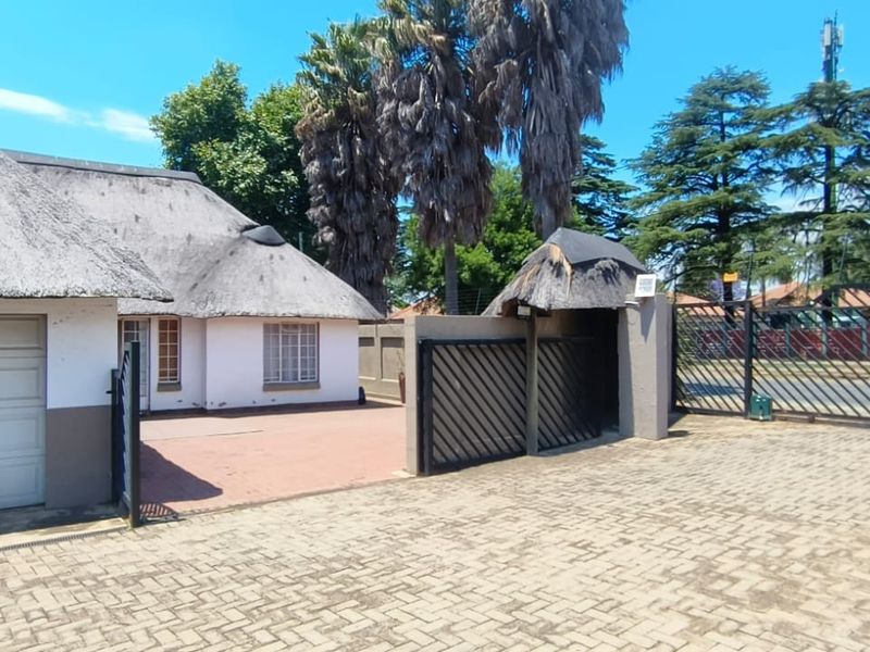 Front exterior view of a property featuring a thatched roof, paved driveway, and secure gated entrance.