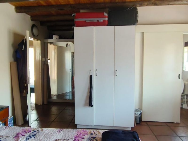 Bedroom featuring exposed timber ceiling beams, tiled flooring, and a built-in wardrobe, with an adjoining en-suite bathroom visible through a sliding door.