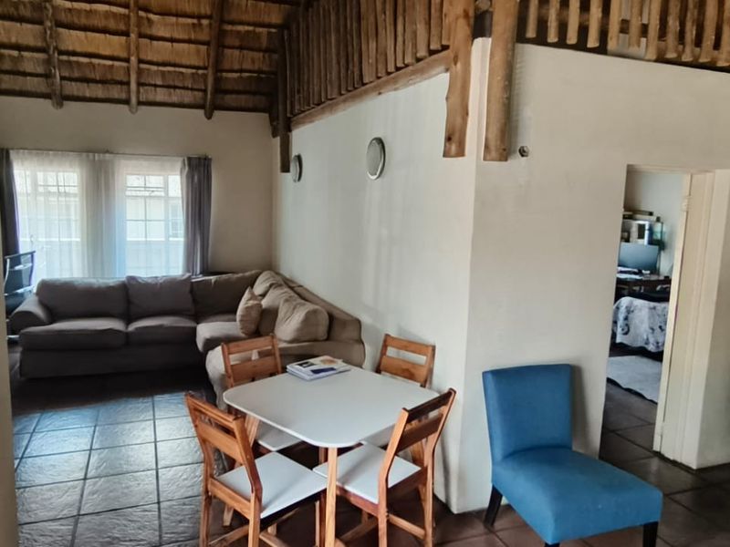 Open-plan living and dining area featuring a high thatched roof with exposed timber beams and tiled flooring, offering a rustic and spacious atmosphere.