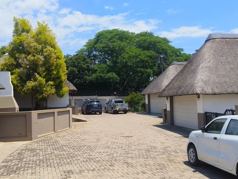 Exterior view of a residential complex featuring multiple units with traditional thatch roofs, paved driveway access, and integrated garage doors.