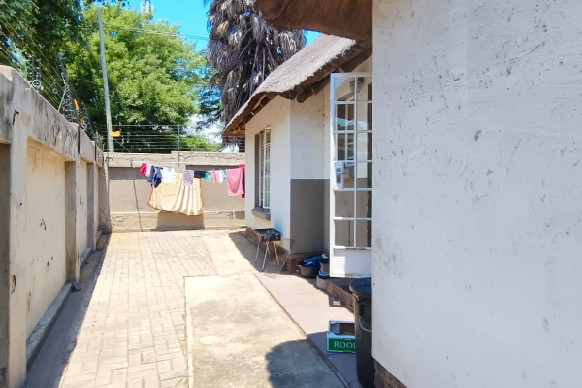 A side exterior view of the property featuring a paved walkway, perimeter wall with electric fencing, and a thatched roof section.
