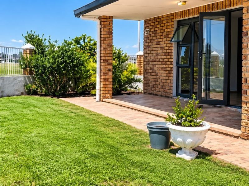 A well-maintained covered brick patio area featuring paved flooring, aluminum door and window frames, and direct access to a private garden space.
