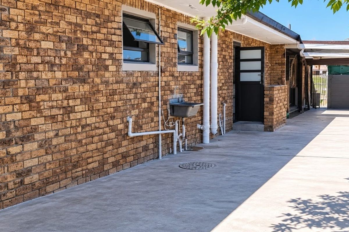 Rear exterior view of the apartment featuring a face brick facade, concrete driveway, utility sink, and secure boundary walling.