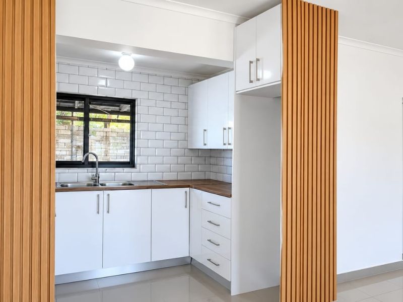 Modern kitchen featuring white cabinetry, wooden countertops, subway tile backsplash, and a stylish slatted wood feature wall.