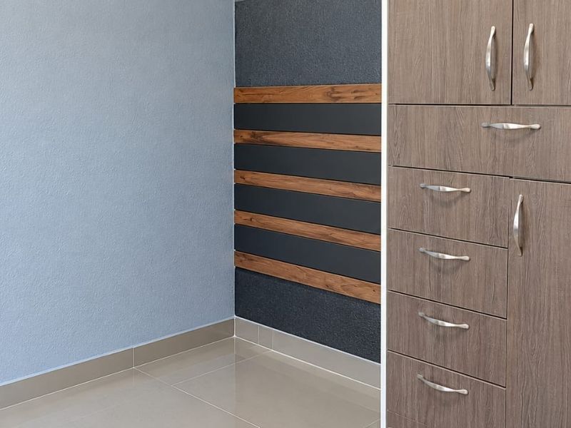 A clean, modern bedroom interior featuring built-in wooden cupboards, tiled flooring, and a stylish decorative accent wall with horizontal paneling.