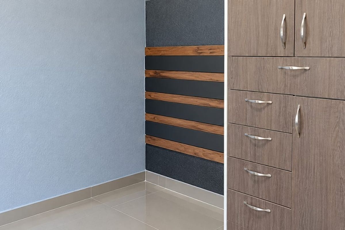 A clean, modern bedroom interior featuring built-in wooden cupboards, tiled flooring, and a stylish decorative accent wall with horizontal paneling.