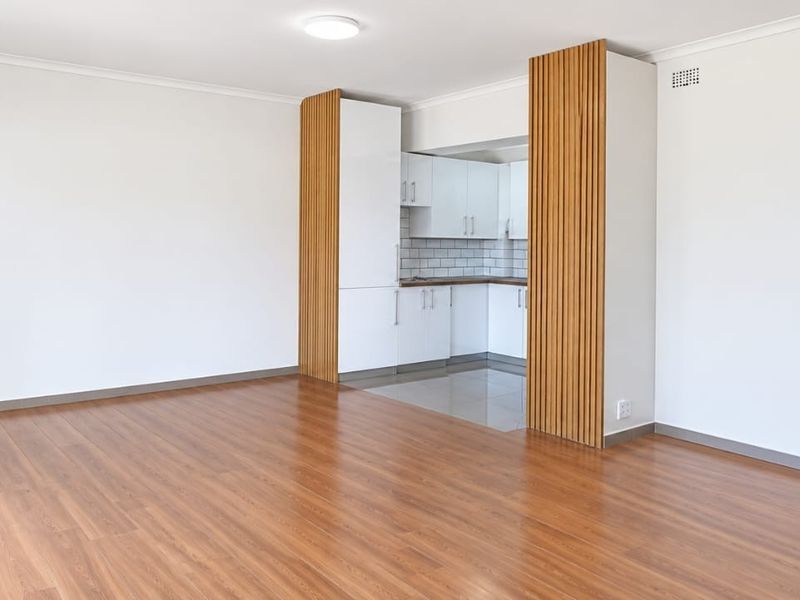 Bright open-plan living area featuring modern laminate flooring, a sleek kitchen with subway tile backsplash, and stylish timber slat feature wall detailing.