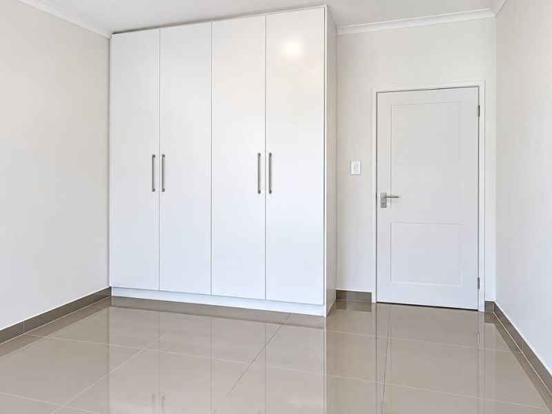 A clean, empty bedroom featuring modern tiled flooring and ample built-in cupboard storage with a neutral white finish.
