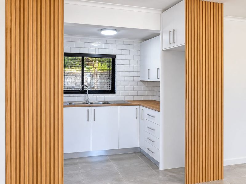 Modern kitchen featuring white cabinetry, timber-look countertops, subway tile backsplash, and a stylish slatted timber feature wall, presented in excellent condition.