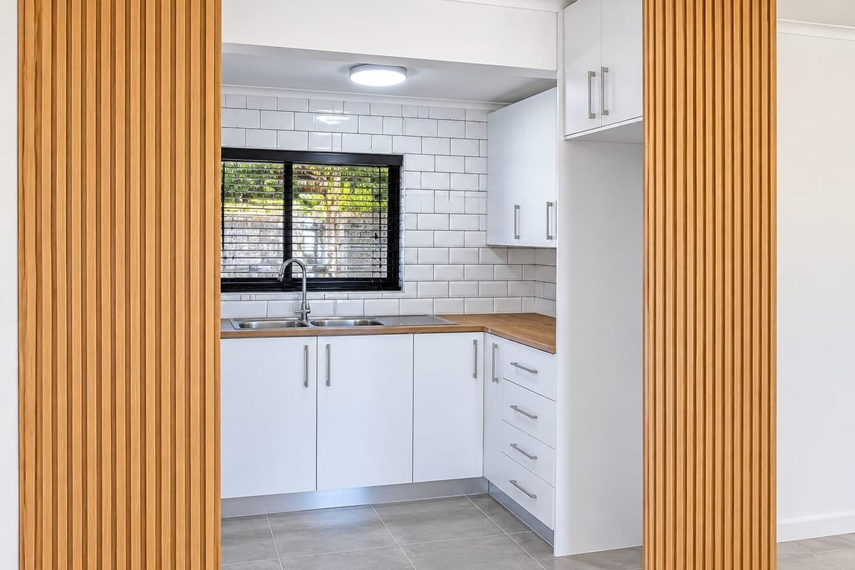 Modern kitchen featuring white cabinetry, timber-look countertops, subway tile backsplash, and a stylish slatted timber feature wall, presented in excellent condition.