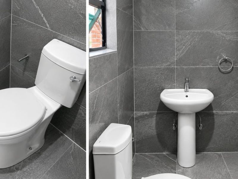 A modern, compact bathroom featuring dark grey stone-look wall and floor tiles, a white pedestal basin, and a matching toilet.