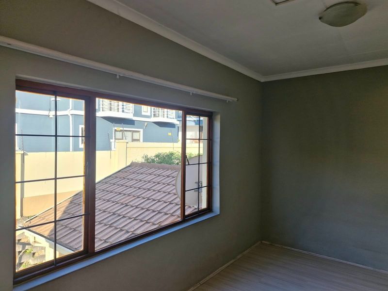 A bright, empty bedroom featuring laminate flooring, a large wooden-framed window, and neutral wall tones, offering a clean canvas for personalization.