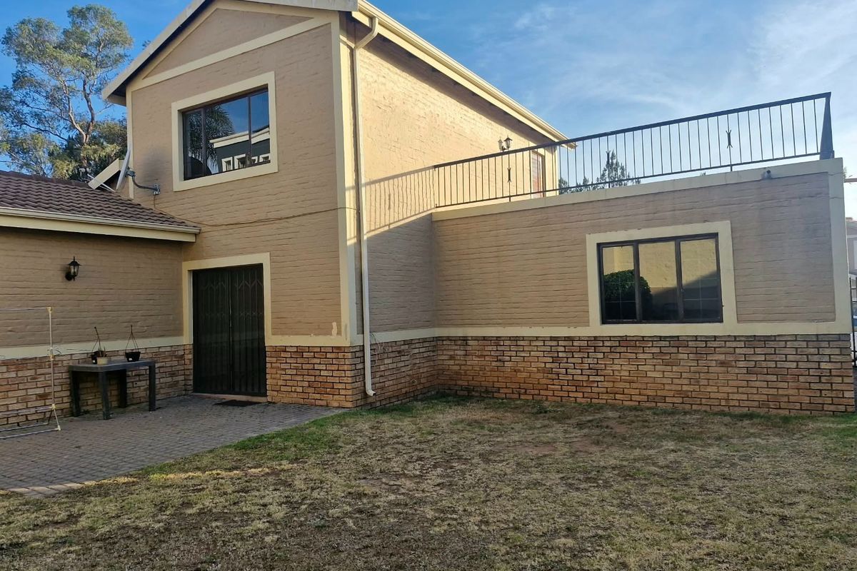 Rear view of a two-story house featuring a paved patio area, brick exterior, and an upper-level balcony with metal railings.