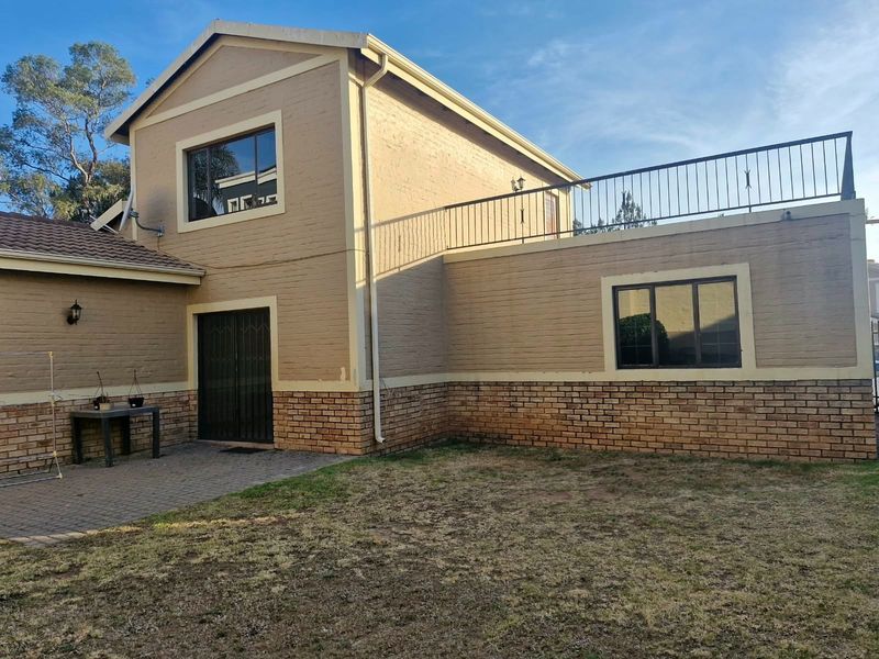 Rear view of a two-story house featuring a paved patio area, brick exterior, and an upper-level balcony with metal railings.