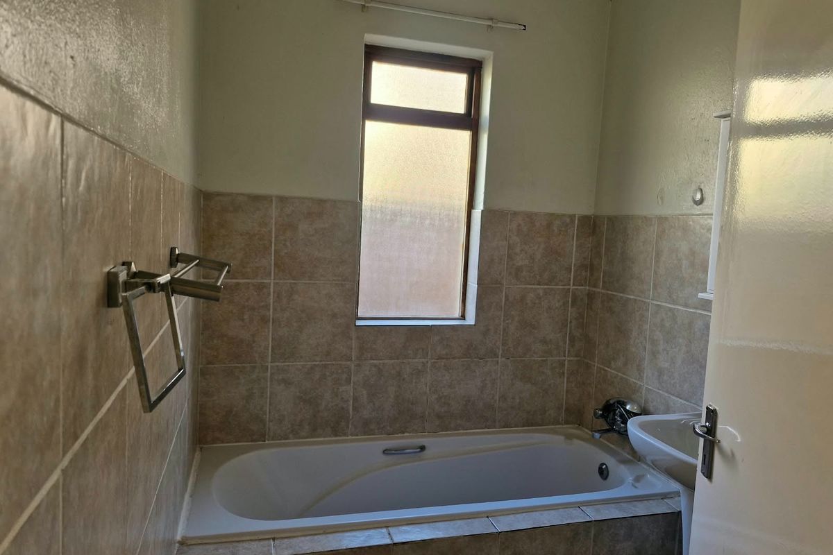 A functional bathroom featuring a built-in bathtub, wall-mounted basin, and neutral tiled splashbacks, offering a clean canvas for potential cosmetic updates.