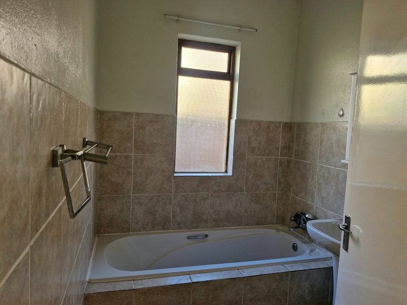 A functional bathroom featuring a built-in bathtub, wall-mounted basin, and neutral tiled splashbacks, offering a clean canvas for potential cosmetic updates.