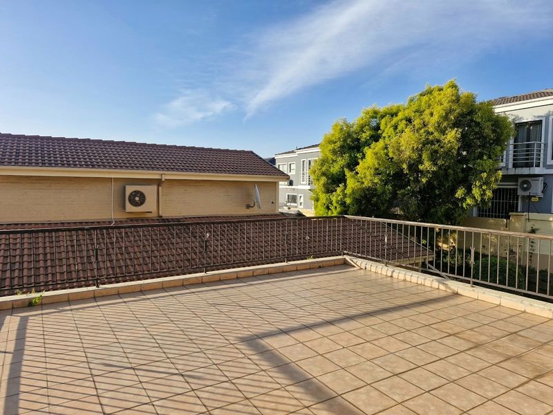 An open-air balcony featuring tiled flooring and a metal balustrade, offering an elevated outdoor space with views of the surrounding residential area.