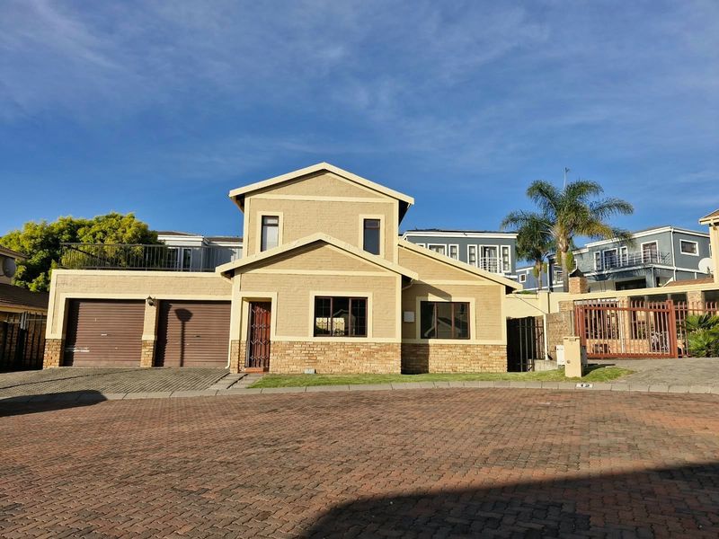 Front elevation of a double-story house featuring a double garage, brick facade, and an upper-level balcony, situated in a paved residential complex.