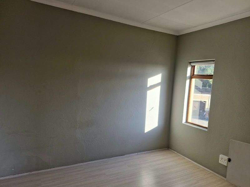 An empty bedroom featuring laminate flooring, a timber-framed window, and neutral wall finishes, offering a blank canvas for personalization.