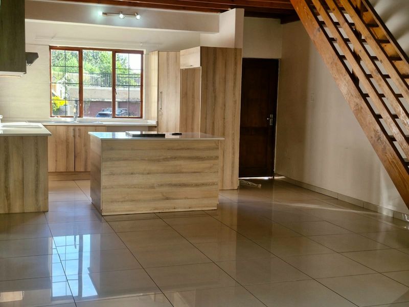 Spacious open-plan kitchen and living area featuring modern wood-finish cabinetry, a central island, tiled floors, and an attractive timber staircase.