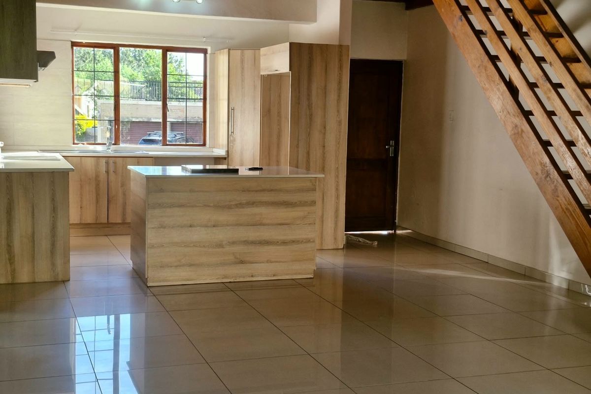 Spacious open-plan kitchen and living area featuring modern wood-finish cabinetry, a central island, tiled floors, and an attractive timber staircase.