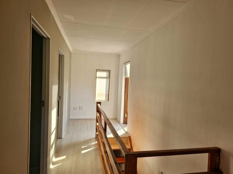 A bright, empty upper-level hallway featuring laminate flooring and a wooden staircase railing, providing access to multiple rooms.