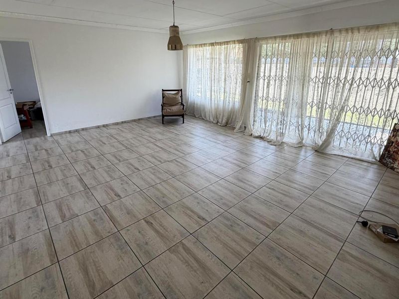 Spacious living area featuring wood-look tiled flooring, large sliding doors with security gates, and neutral wall finishes.