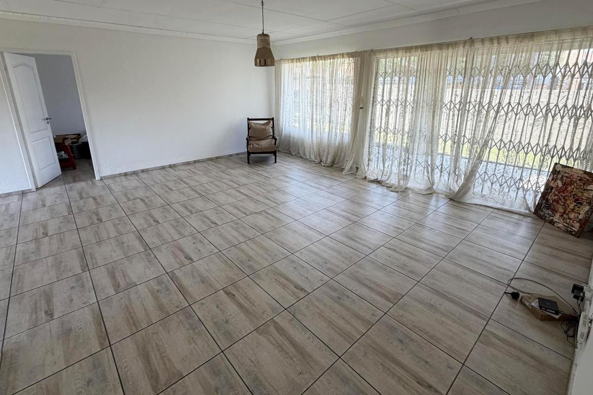 Spacious living area featuring wood-look tiled flooring, large sliding doors with security gates, and neutral wall finishes.